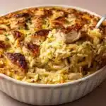 A close-up of a creamy chicken orzo bake casserole with golden-brown chicken pieces and fresh parsley, being served with a spoon.