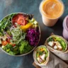 Overhead view of a colorful healthy fast food meal featuring a fresh vegetable salad, grilled chicken wraps, and fruit smoothies on a rustic table