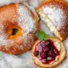 Overhead view of two golden vegan cottage cheese bagels, one sliced with berries and mint, on a light wooden surface