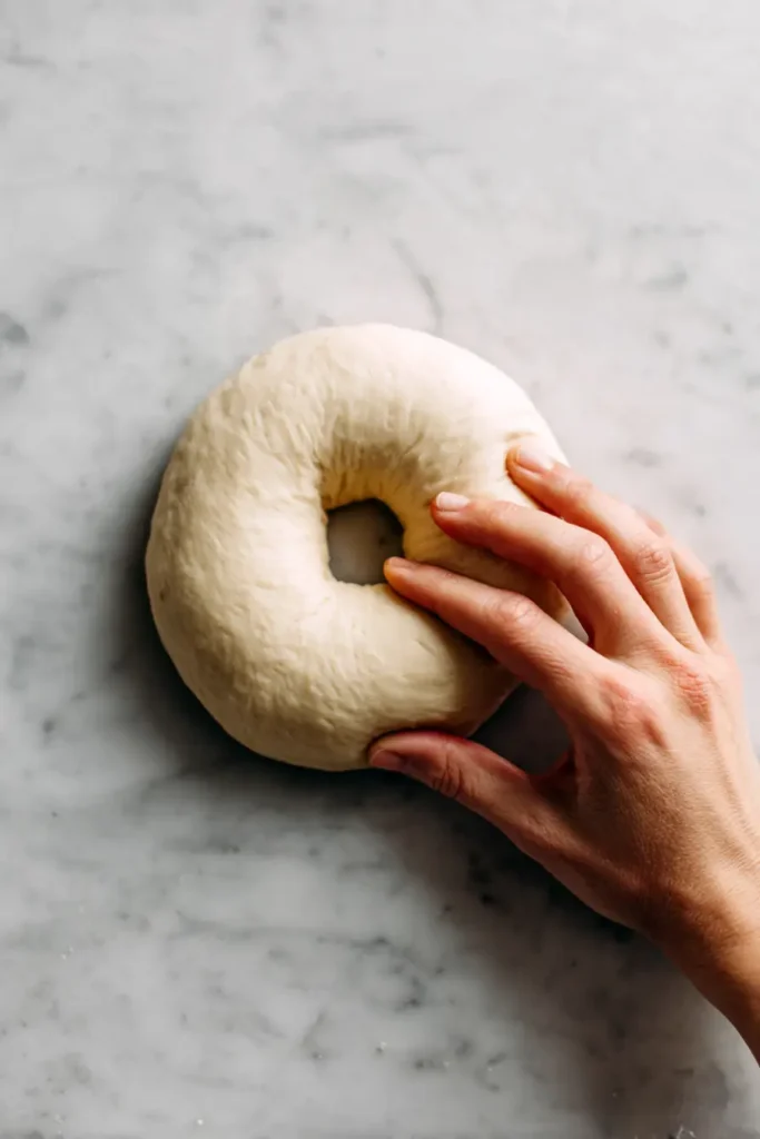 Hands gently shaping a round **plant-based cottage cheese bagel** dough on a marble surface.